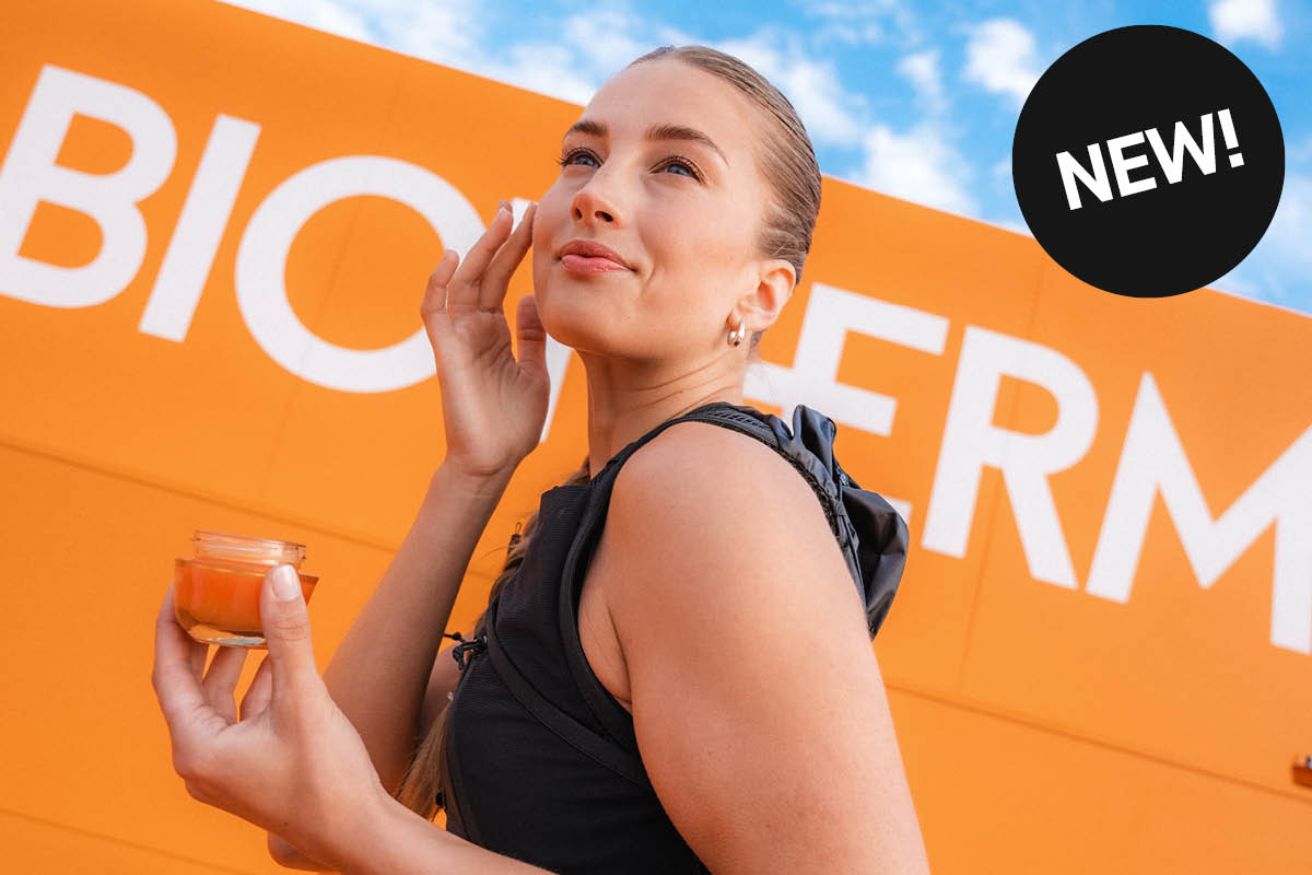 En person holder en oransje Biotherm-krukke foran en lys bakgrunn.
