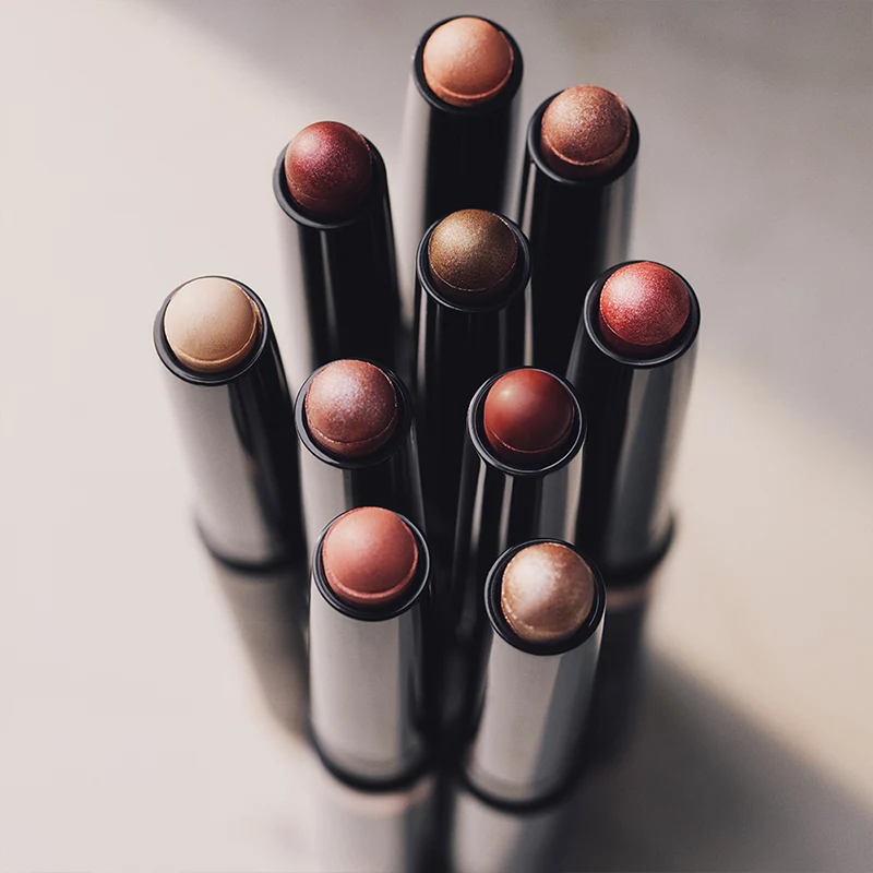 Ni skimrende sminkestifter i forskjellige varme og nøytrale toner som bronse, roségull og beige.