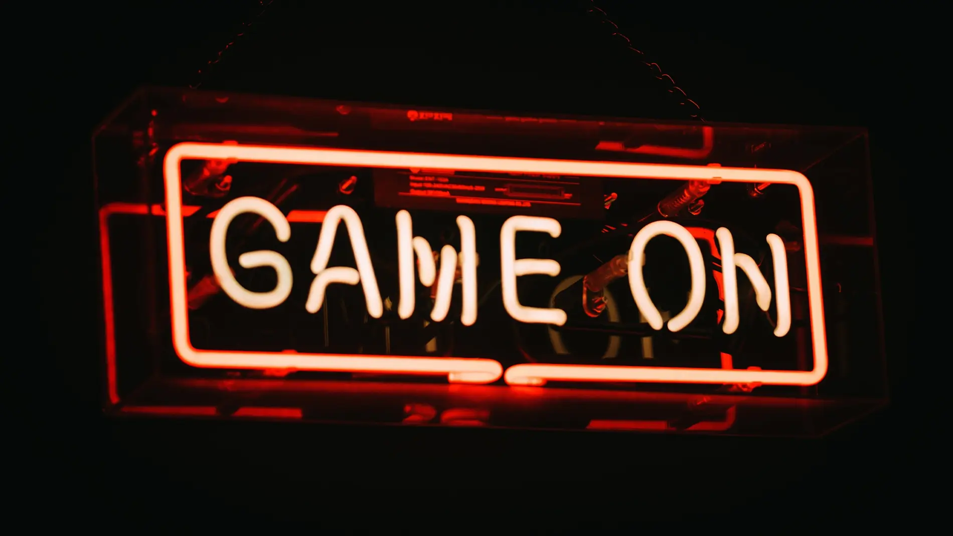 Rødt og hvitt neonskilt med teksten “GAME ON” mot mørk bakgrunn. Det opplyste skiltet gir en moderne og intens gamingstemning.