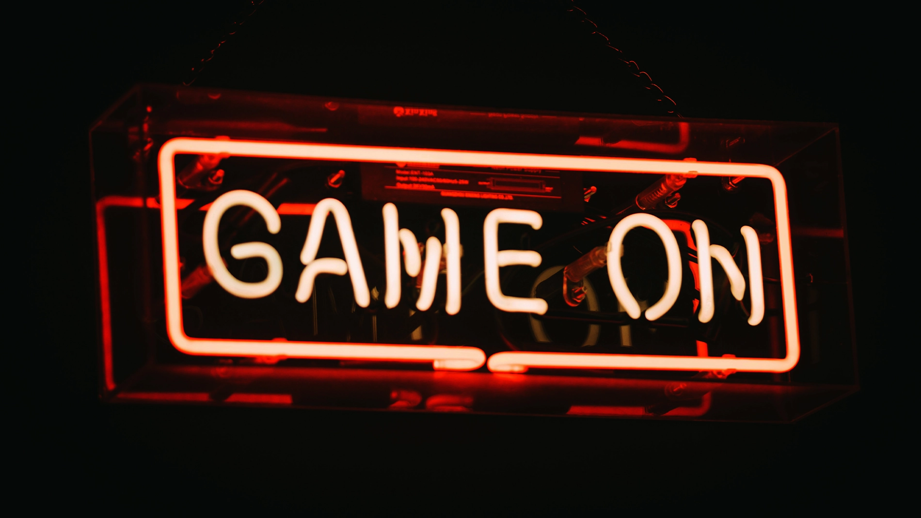 Röd och vit neonsskylt med texten “GAME ON” mot mörk bakgrund. Den upplysta skylten ger en modern och intensiv gamingkänsla.