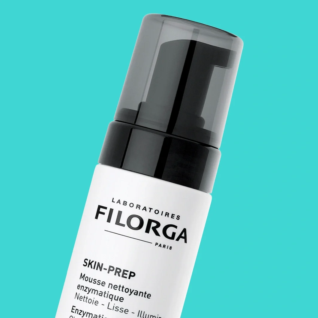 Filorga Skin-Prep Mousse Nettoyante Enzymatique -puhdistusvaahto valkoisessa pumppupullossa turkoosia taustaa vasten. Pakkauksessa näkyvät tekstit "LABORATOIRES FILORGA PARIS", "SKIN-PREP", "Mousse Nettoyante Enzymatique", "Nettoie - Lisse - Illumine" ja "Enzymatic Cleansing Foam".