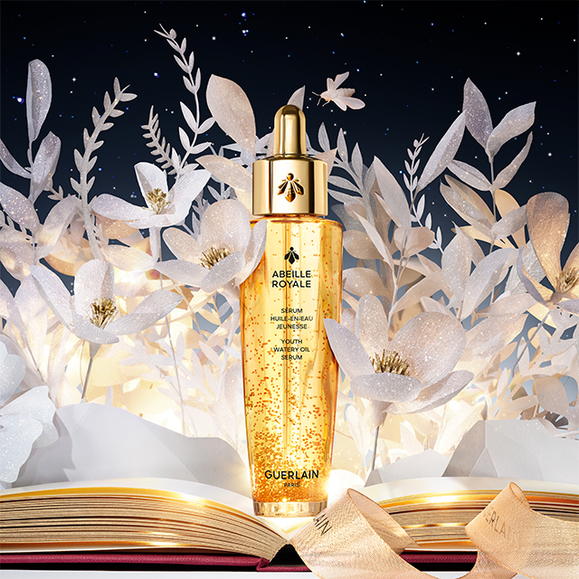 En flaska av Guerlain Abeille Royale Youth Watery Oil Serum mot en vit bakgrund. Flaskan är gyllene och genomskinlig, med en elegant guldkork och en pipett för applicering. Flaskan har en lyxig och sofistikerad design.
