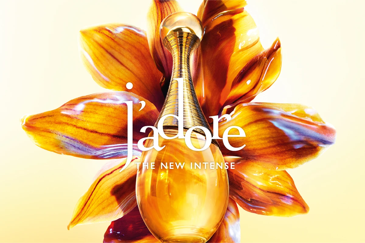 Dior J’adore -hajuvesipullo suuren kultaisen kukan edessä, kuvassa teksti “j’adore” ja “THE NEW INTENSE”.