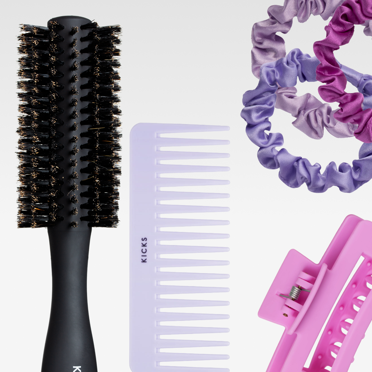 Hårtillbehör mot vit bakgrund: rundborste, bredtandad kam, tygscrunchies i lila nyanser och en rosa hårklämma.
