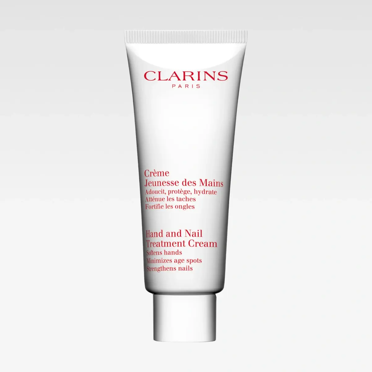 Vit tub från Clarins med röd text “CLARINS PARIS” och “Crème Jeunesse des Mains”. Texten beskriver “Hand and Nail Treatment Cream, softens hands, minimizes age spots, strengthens nails”.