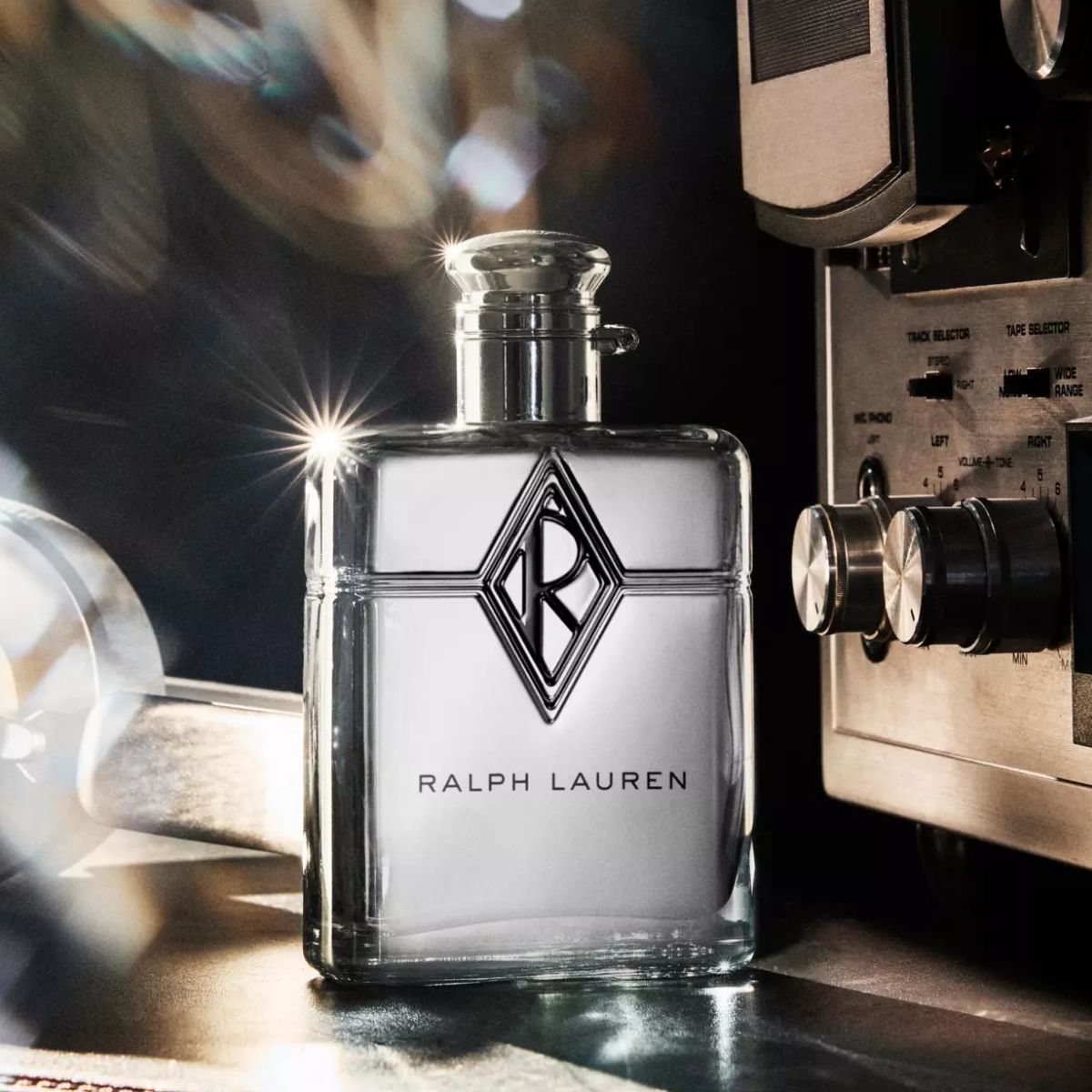 Ralph Lauren parfymeflaske på en blank overflate, med retro lydutstyr og lysrefleksjoner i bakgrunnen.