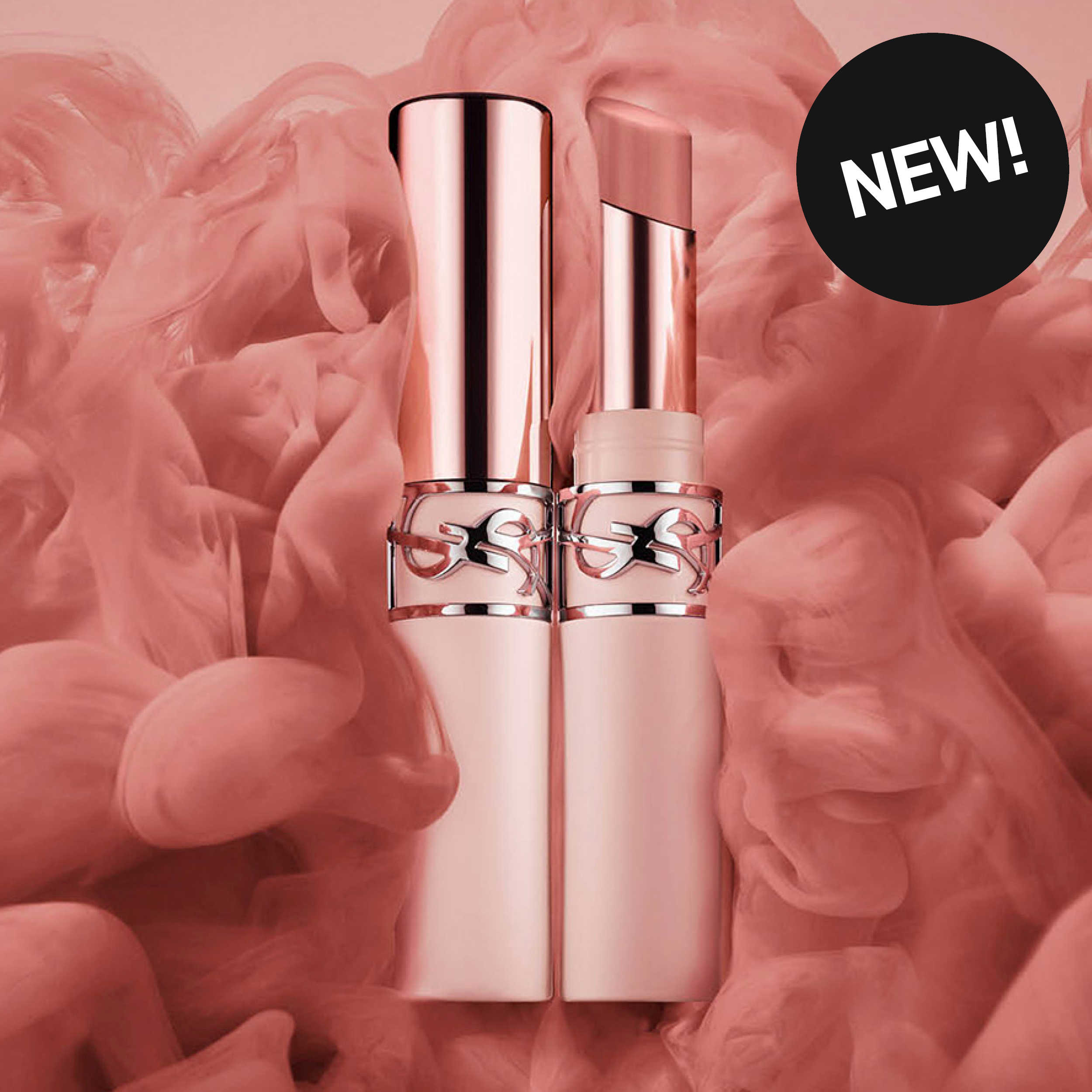 Kaksi YSL-huulituotetta ruusukullan sävyisessä pakkauksessa on vaaleanpunaista pilvimäistä taustaa vasten. Pakkauksessa on YSL-logo ja musta ympyrä tekstillä “NEW!”.