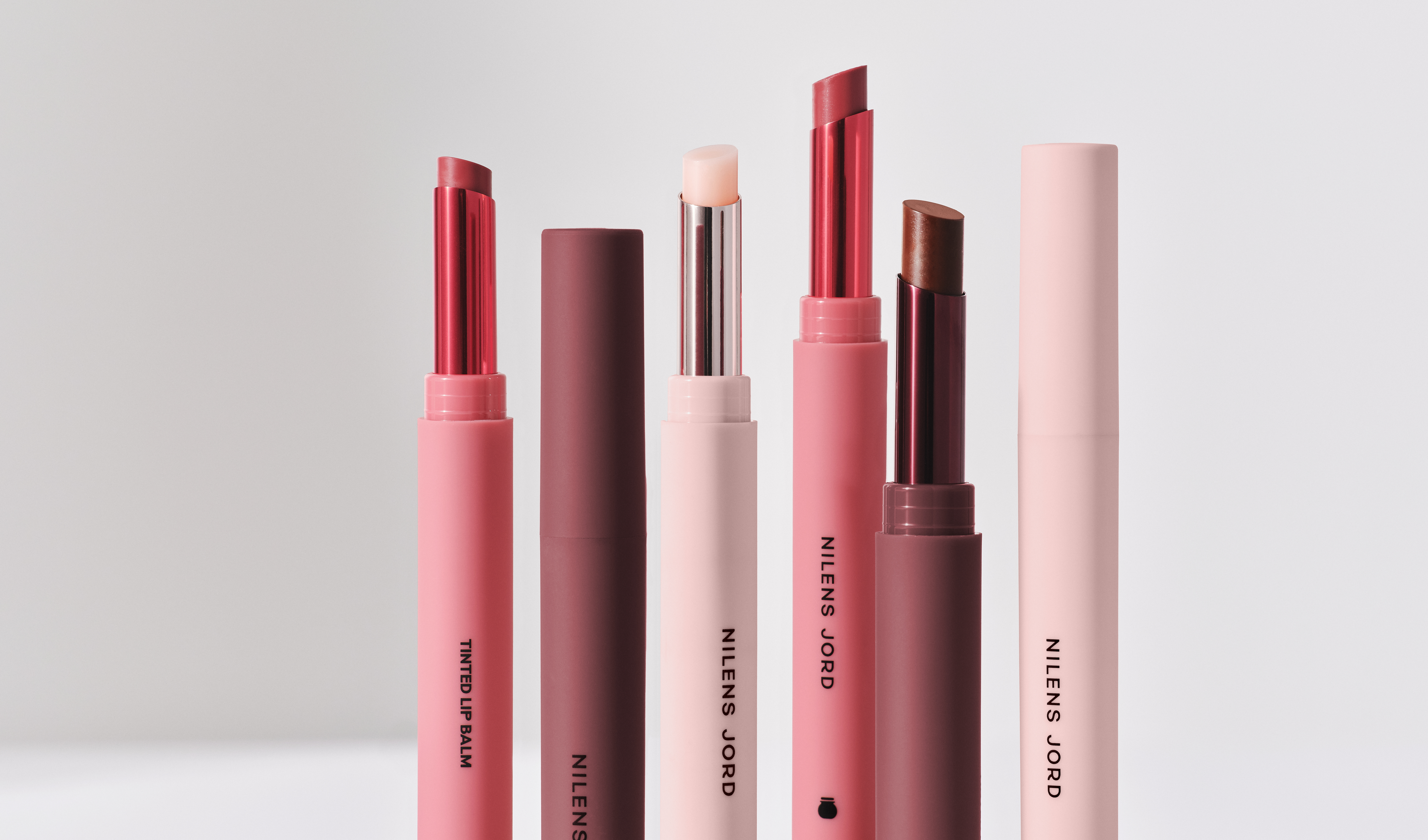 Flere leppebalmer fra Nilens Jord i ulike nyanser, arrangert stående mot en lys, nøytral bakgrunn.