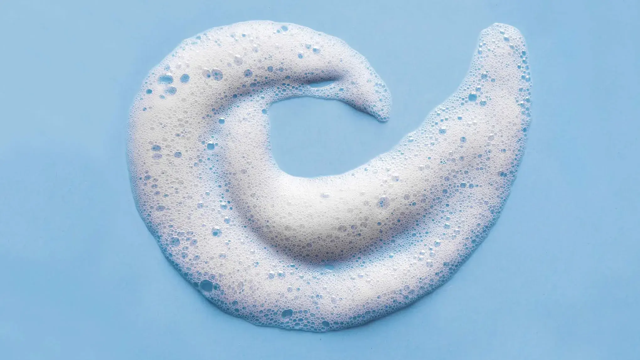 Hvitt skum med bobler formet som en spiral, på en blå overflate.