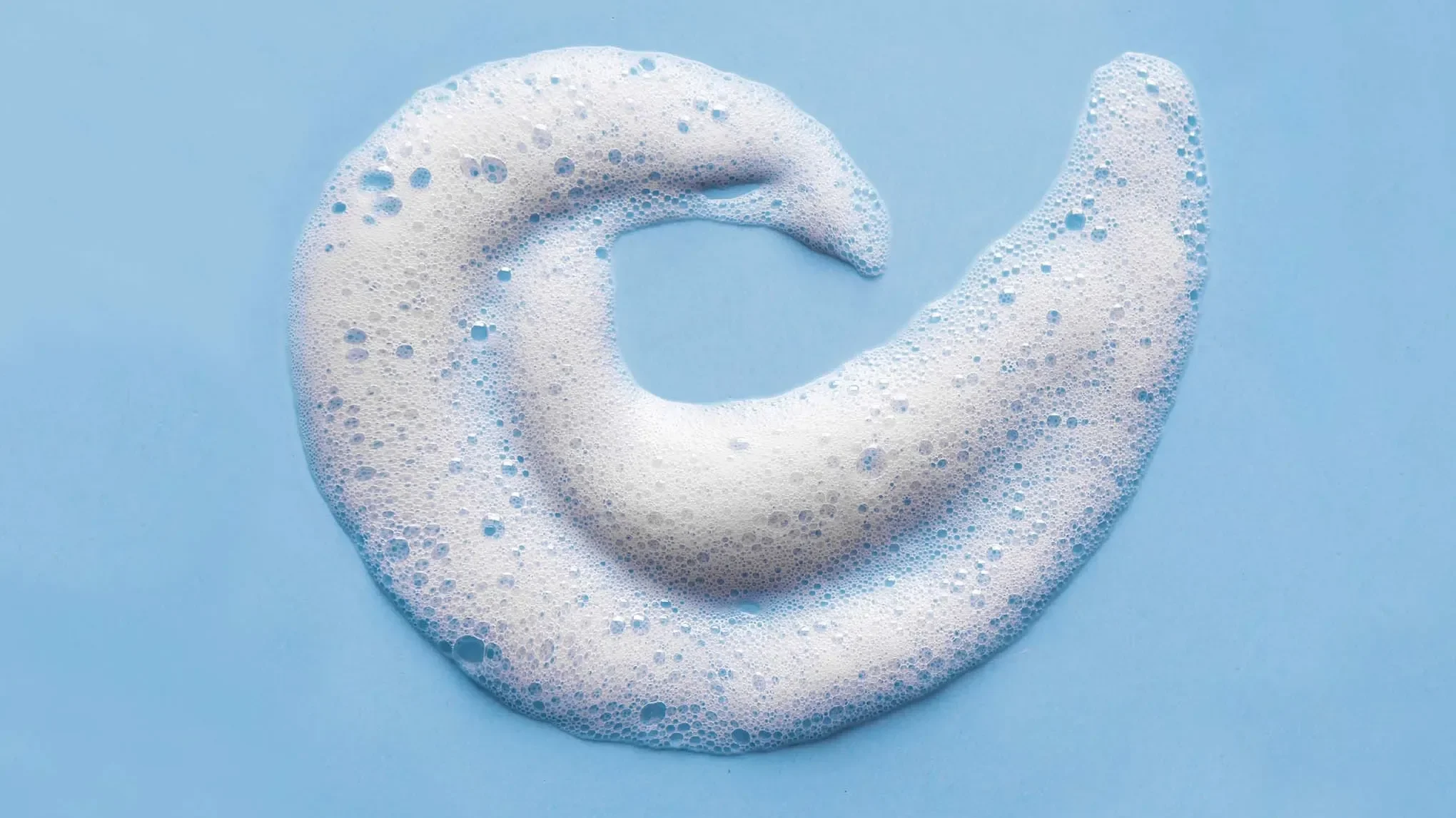 Vitt skum med bubblor format som en spiral, mot ett blått underlag.