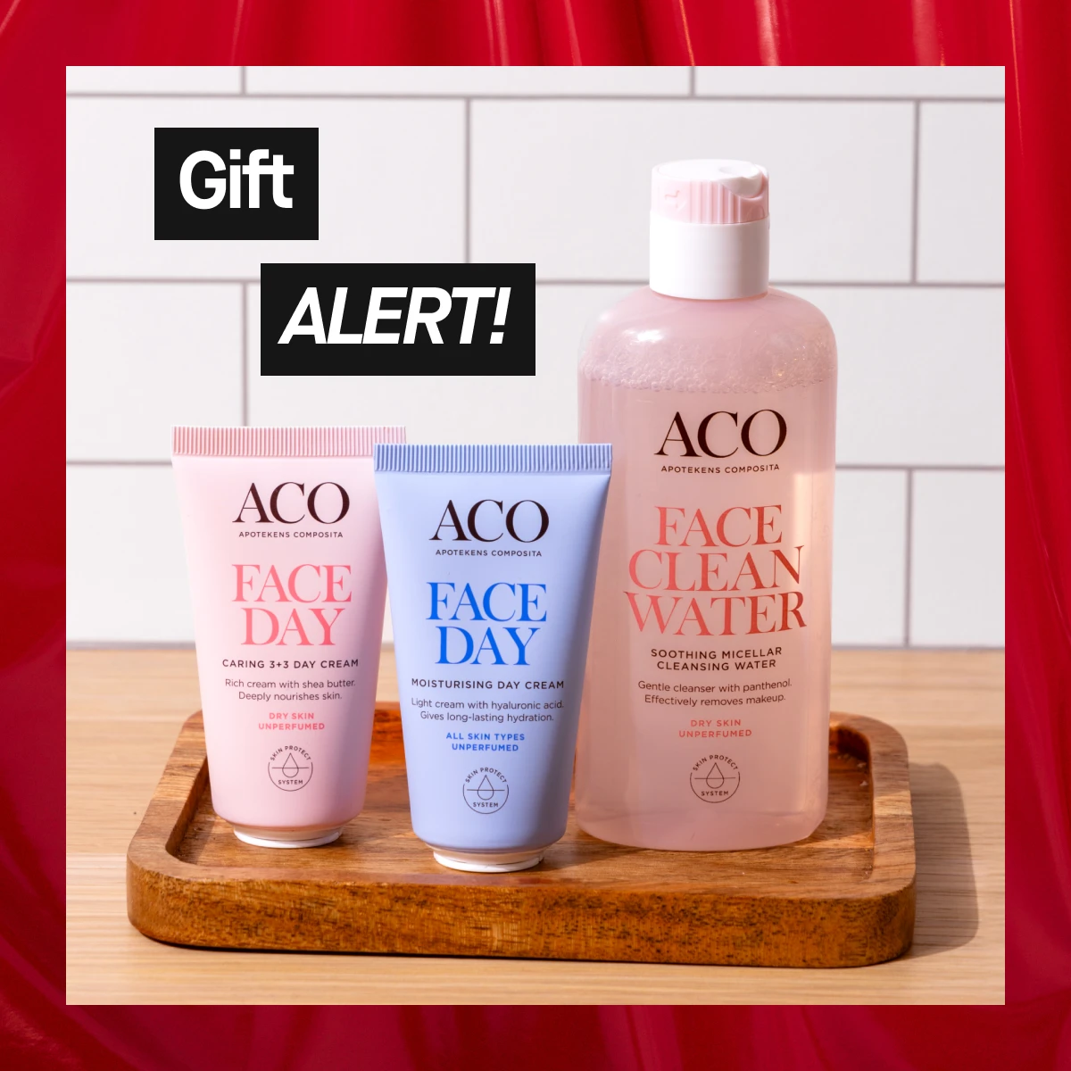 Bild som visar tre ACO produkter: Face Day Caring 3+3 Day Cream, Face Day Moisturising Day Cream, och Face Clean Water. Texten "Gift ALERT!" är synlig. Bakgrunden är vit med röda detaljer.