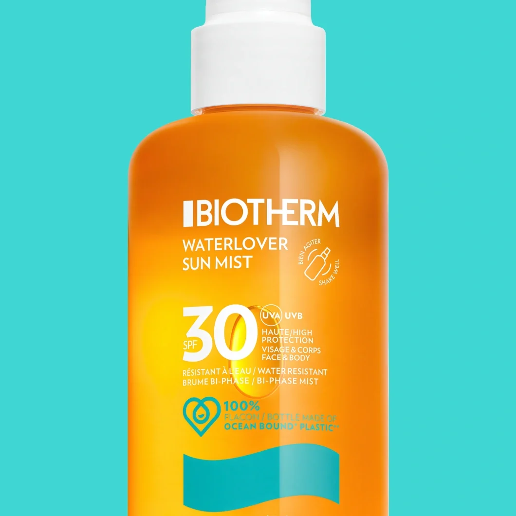 Biotherm Waterlover Sun Mist SPF 30 solspray i en oransje flaske mot turkis bakgrunn. På emballasjen står tekstene «BIOTHERM», «WATERLOVER SUN MIST», «SPF 30», «UVA UVB», «HIGH PROTECTION», «FACE & BODY», «WATER RESISTANT BI-PHASE MIST», «SHAKE WELL» og «100% BOTTLE MADE OF OCEAN BOUND PLASTIC».