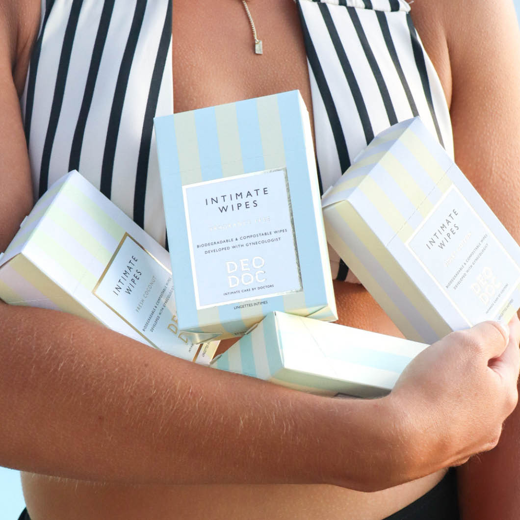 Nainen, joka pitelee useita DeoDoc Intimate Wipes -pakkauksia. Hänellä on yllään mustavalkoraidallinen yläosa.