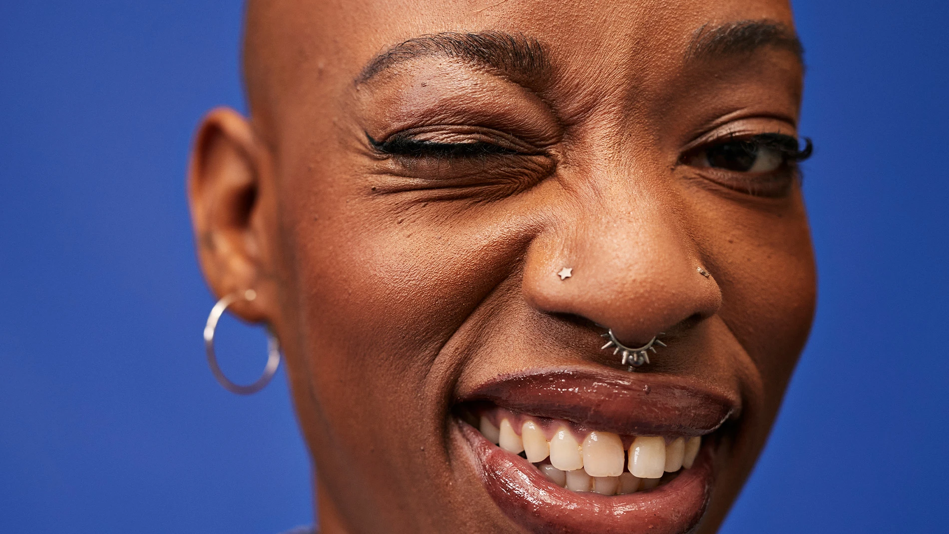 Person med blå bakgrund, silverörhänge och näspiercing.