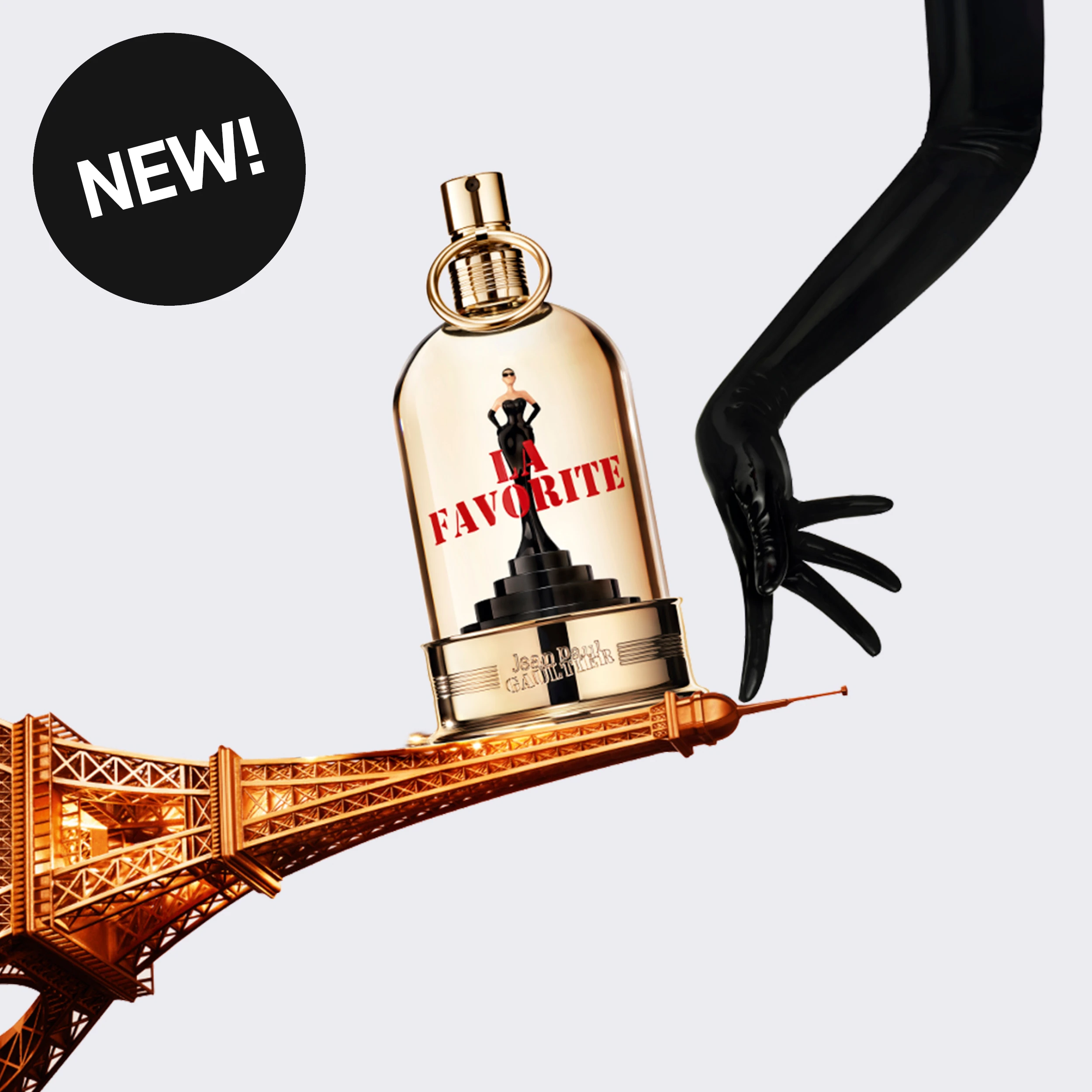 NEW! Jean Paul Gaultier La Favorite -hajuvesi kullanvärisessä pullossa, jossa lukee “LA FAVORITE”, kullanvärisen Eiffel-tornirakennelman yläpuolella mustahansikkaisen käden vieressä.