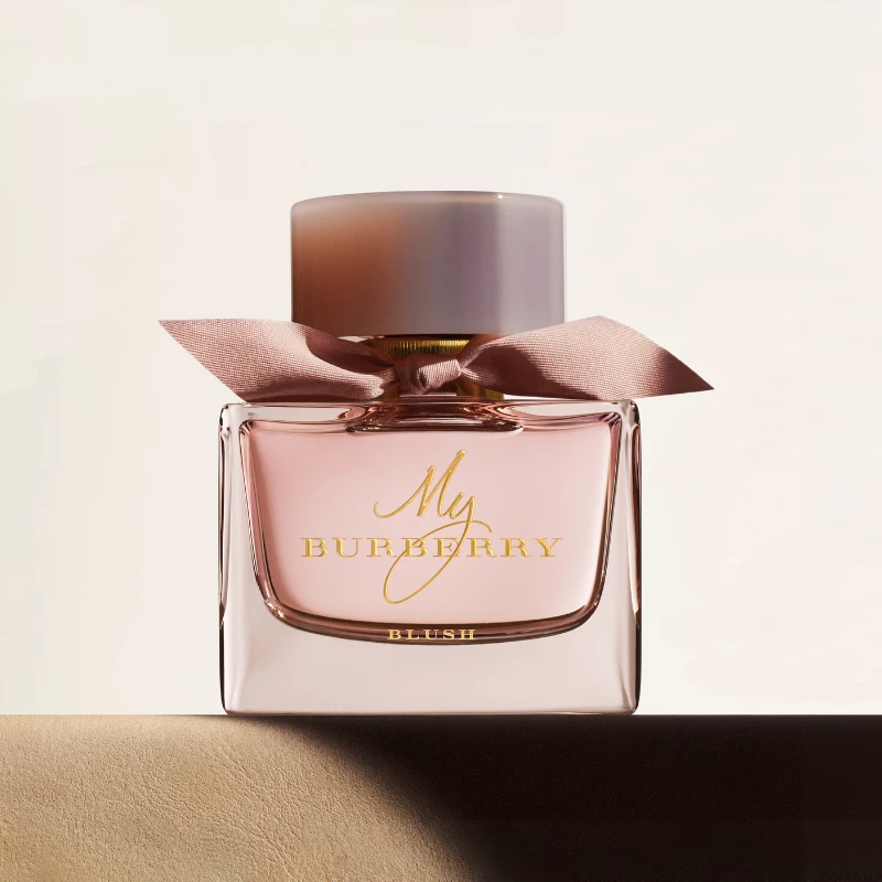 Burberryn hajuvesipullo nimeltä ”My Burberry Blush”, joka on koristeltu vaaleanpunaisella rusetilla ja asetettu vaalealle alustalle.