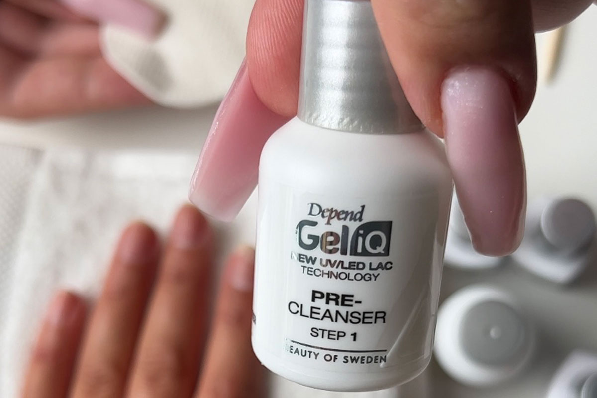 Närbild av en hand som håller i en flaska nagelrengöringsmedel med en nagelberedningsscen i bakgrunden.