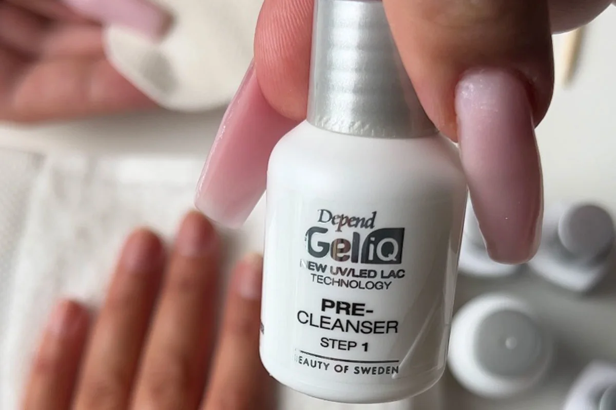 Närbild av en hand som håller i en flaska nagelrengöringsmedel med en nagelberedningsscen i bakgrunden.
