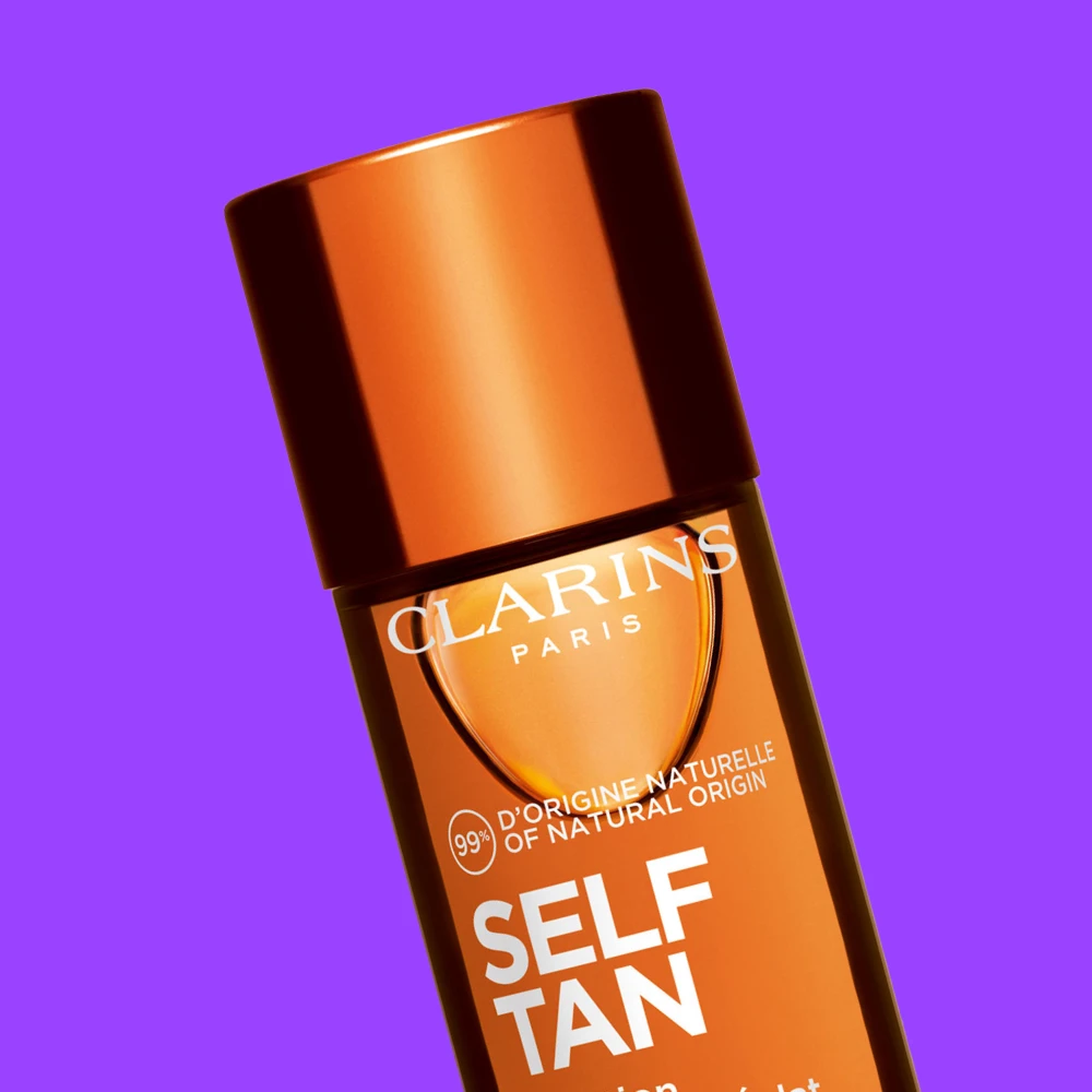 Clarins Paris Self Tan itseruskettava voide oranssissa pullossa violettia taustaa vasten.