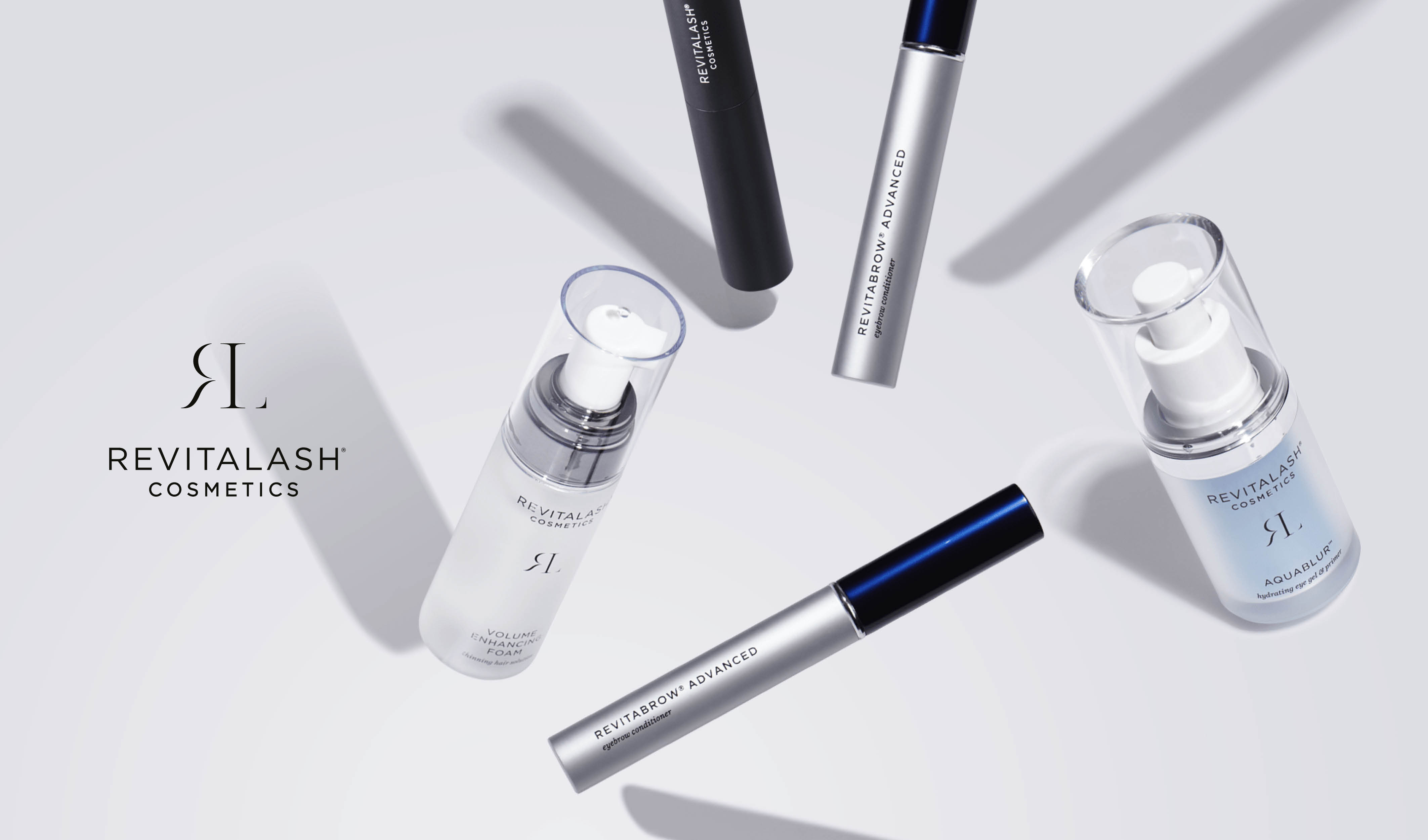 Revitalash Cosmeticsin kauneustuotteiden kokoelma on järjestetty vaaleanharmaalle taustalle. Kuvan vasemmalla puolella on tuotemerkin logo ja teksti ”Revitalash Cosmetics”. Tuotteilla on tyylikkäät pakkaukset, joiden värit ovat valkoinen, musta ja hopea.