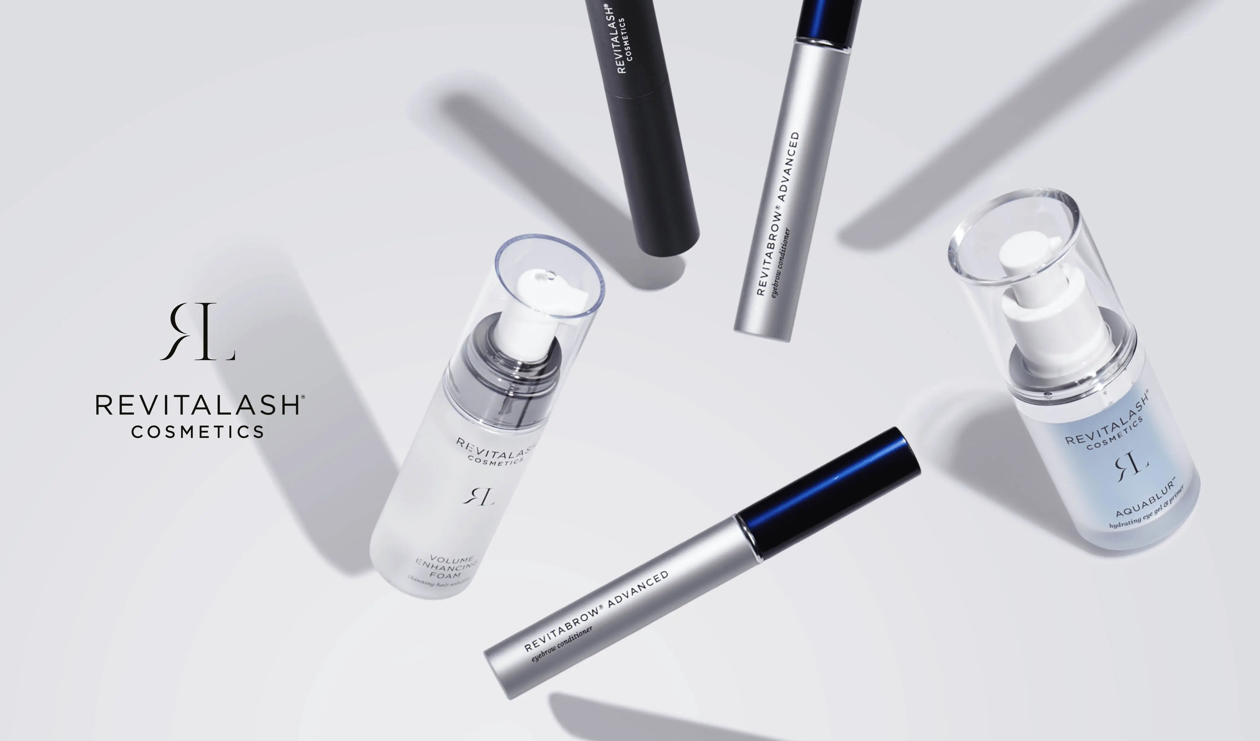 Revitalash Cosmeticsin kauneustuotteiden kokoelma on järjestetty vaaleanharmaalle taustalle. Kuvan vasemmalla puolella on tuotemerkin logo ja teksti ”Revitalash Cosmetics”. Tuotteilla on tyylikkäät pakkaukset, joiden värit ovat valkoinen, musta ja hopea.