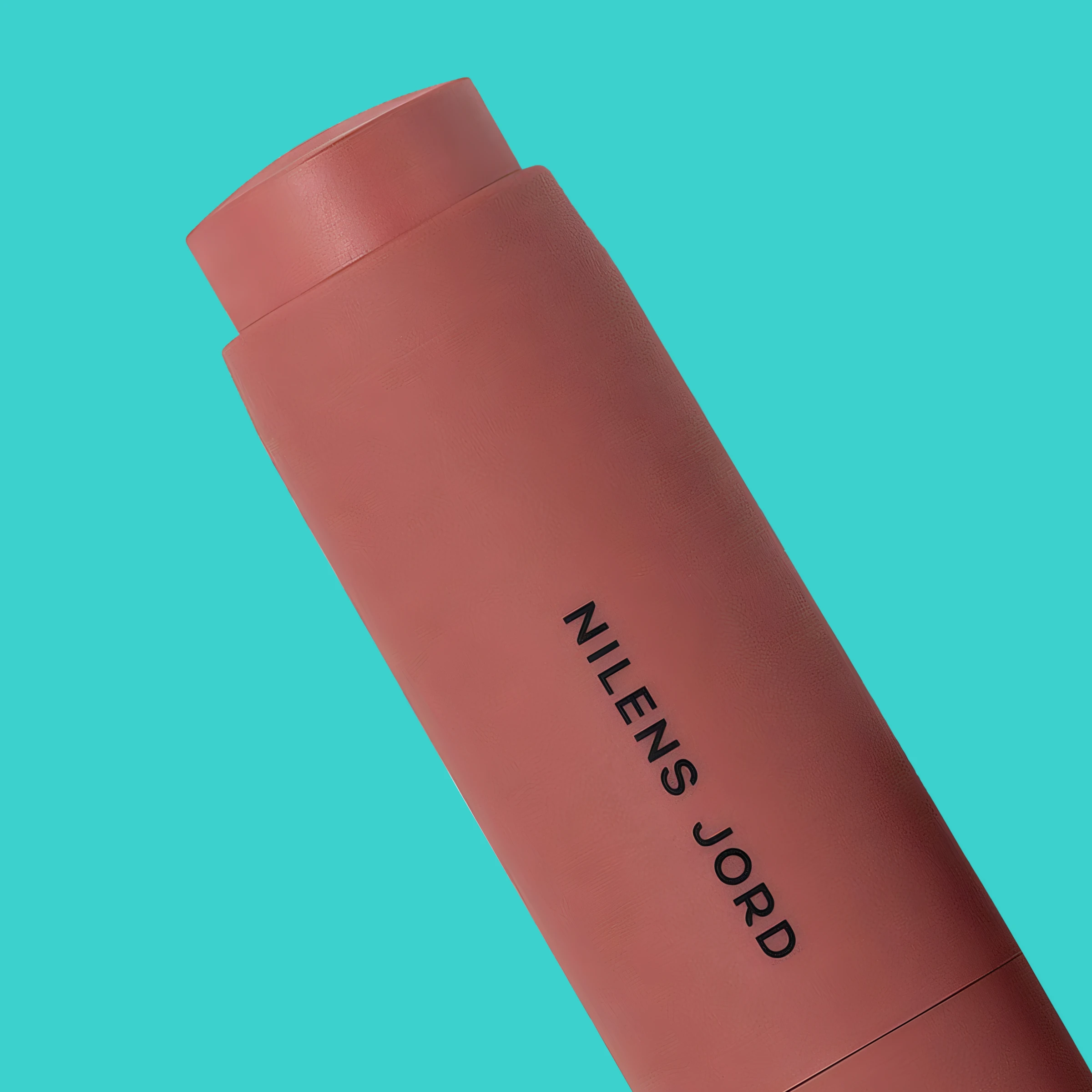 Produktbilde av kremrouge i stiftform mot turkis bakgrunn. Sylinderformet emballasje i varm rosa nyanse.