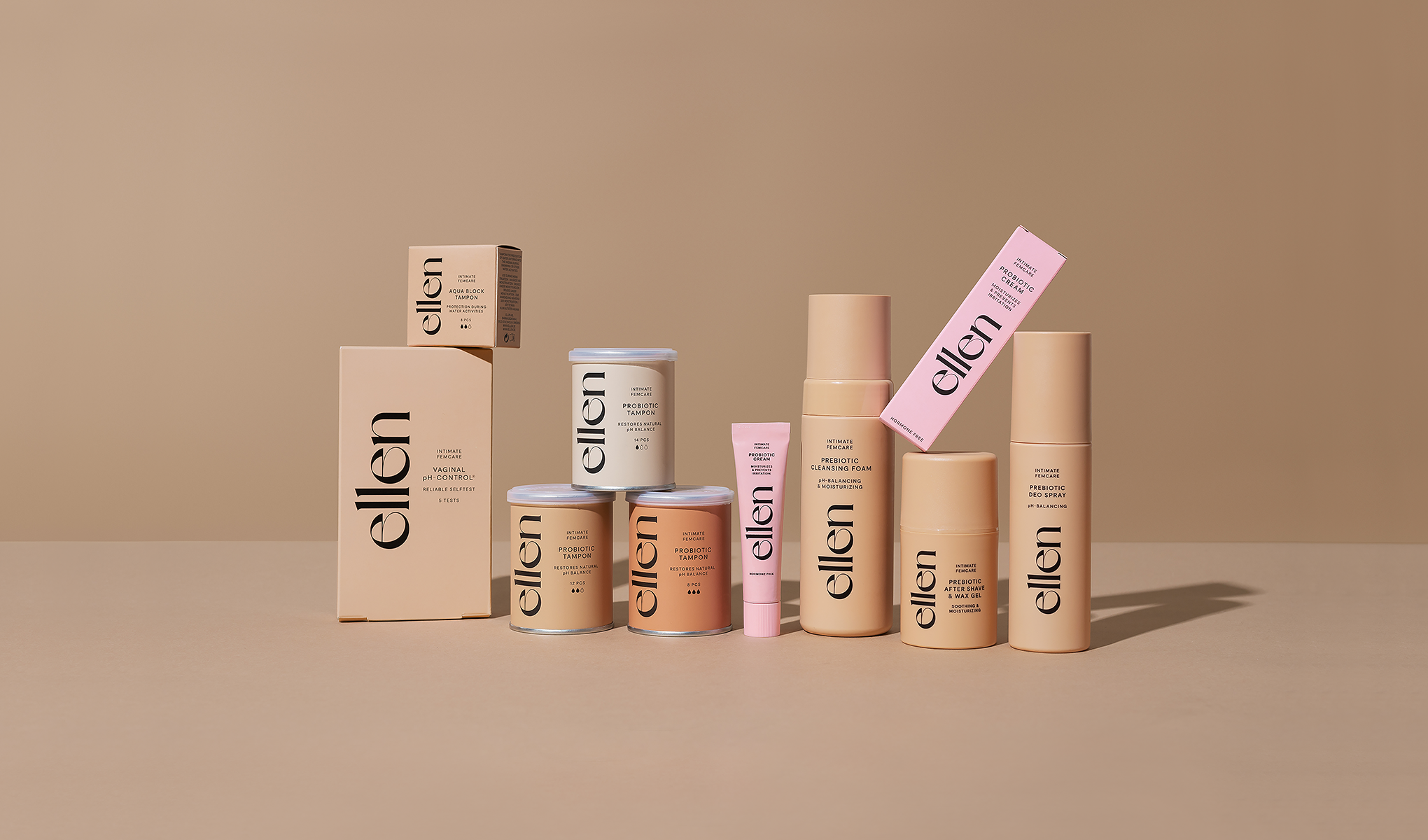 Produktoppsett av intimpleieprodukter fra ellen på beige bakgrunn, inkludert “Intimate Cleanser pH Control”, “Probiotic Tampon”, “Aqua Block Tampon” og “Prebiotic Deo Spray” samt “Prebiotic Cleansing Foam” og “After Shave & Wax Gel”. Emballasje i nøytrale toner med rosa detaljer og tydelig ellen-logo.