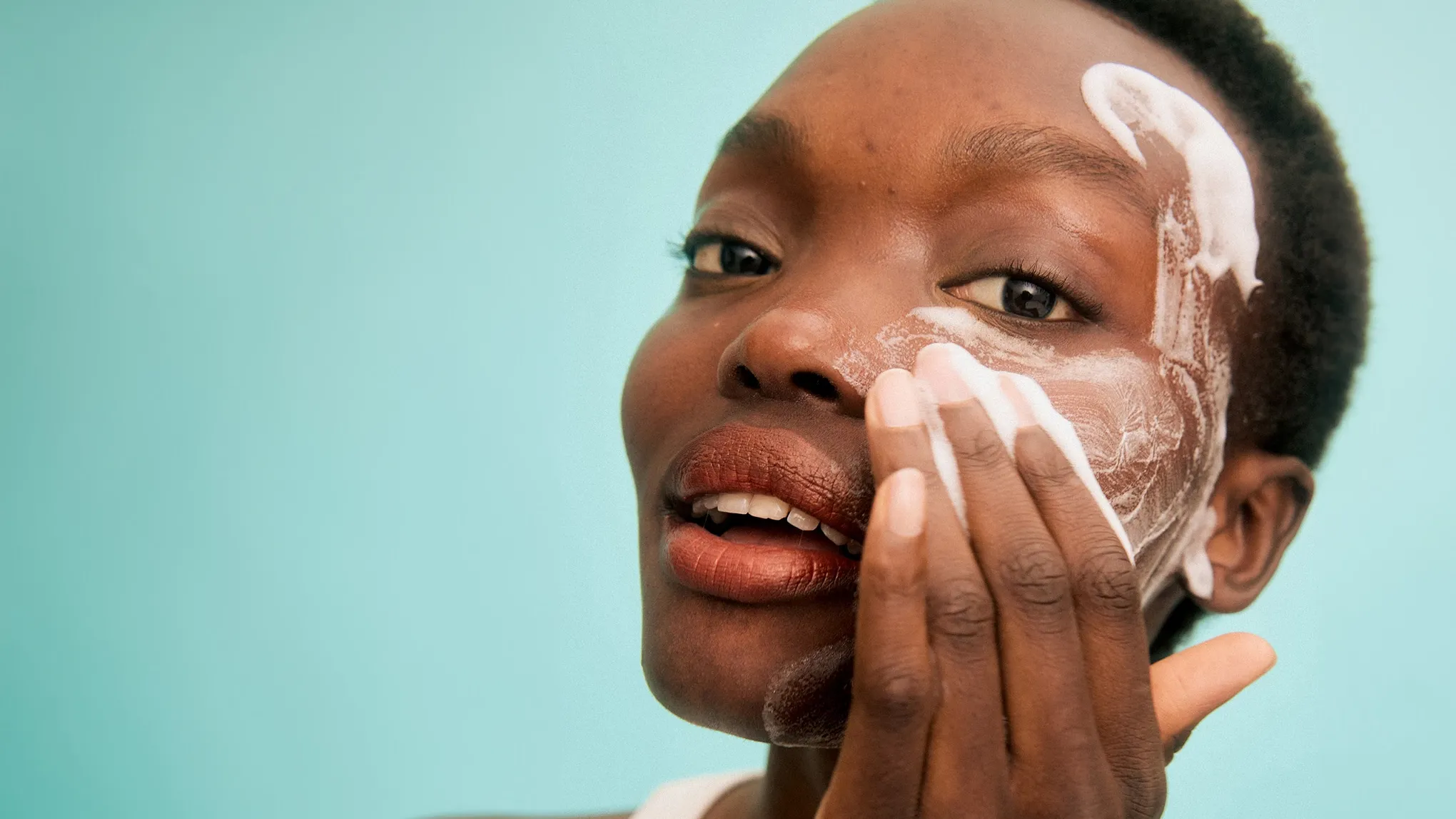 Kvinna smörjer in kinden med peeling. Studioporträtt med turkos bakgrund.