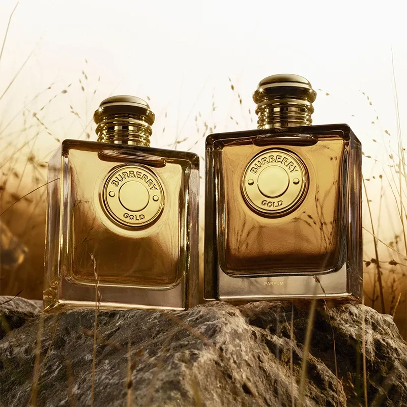 Två parfymer från Burberry med namnet "Burberry Goddess", placerade på en stenig yta med en suddig naturlig bakgrund.