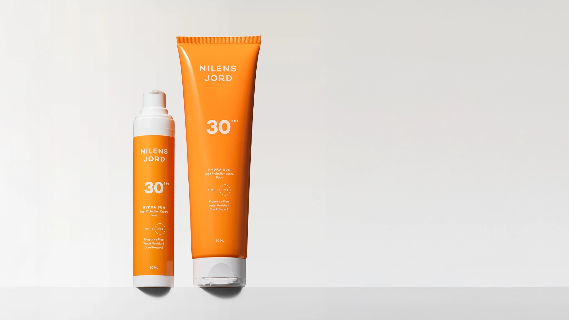 To oransje solkremprodukter fra Nilens Jord Hydra Sun SPF 30 står mot en lys bakgrunn. Emballasjen viser teksten “Nilens Jord”, “30 SPF”, “Hydra Sun”, “High Protection Cream”, “High Protection Lotion Body”, “UVB + UVA”, “Fragrance Free”, “Water Resistant”, “Coral Respect”, samt størrelsene 50 ML og 150 ML.