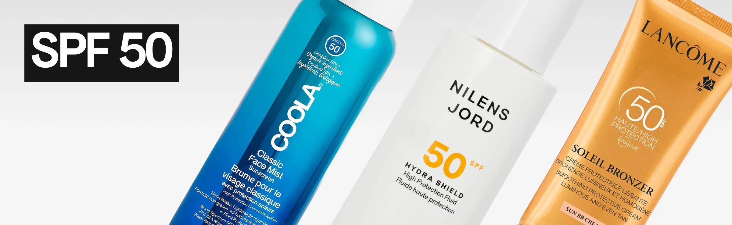 Useita aurinkosuojatuotteita vaaleaa taustaa vasten ja teksti “SPF 50” valkoisella mustalla taustalla vasemmalla. Näkyvissä ovat Coola Classic Face Mist SPF 50 -suihke, Nilens Jord Hydra Shield SPF 50 -pullo ja Lancôme Soleil Bronzer SPF 50 -tuubi.