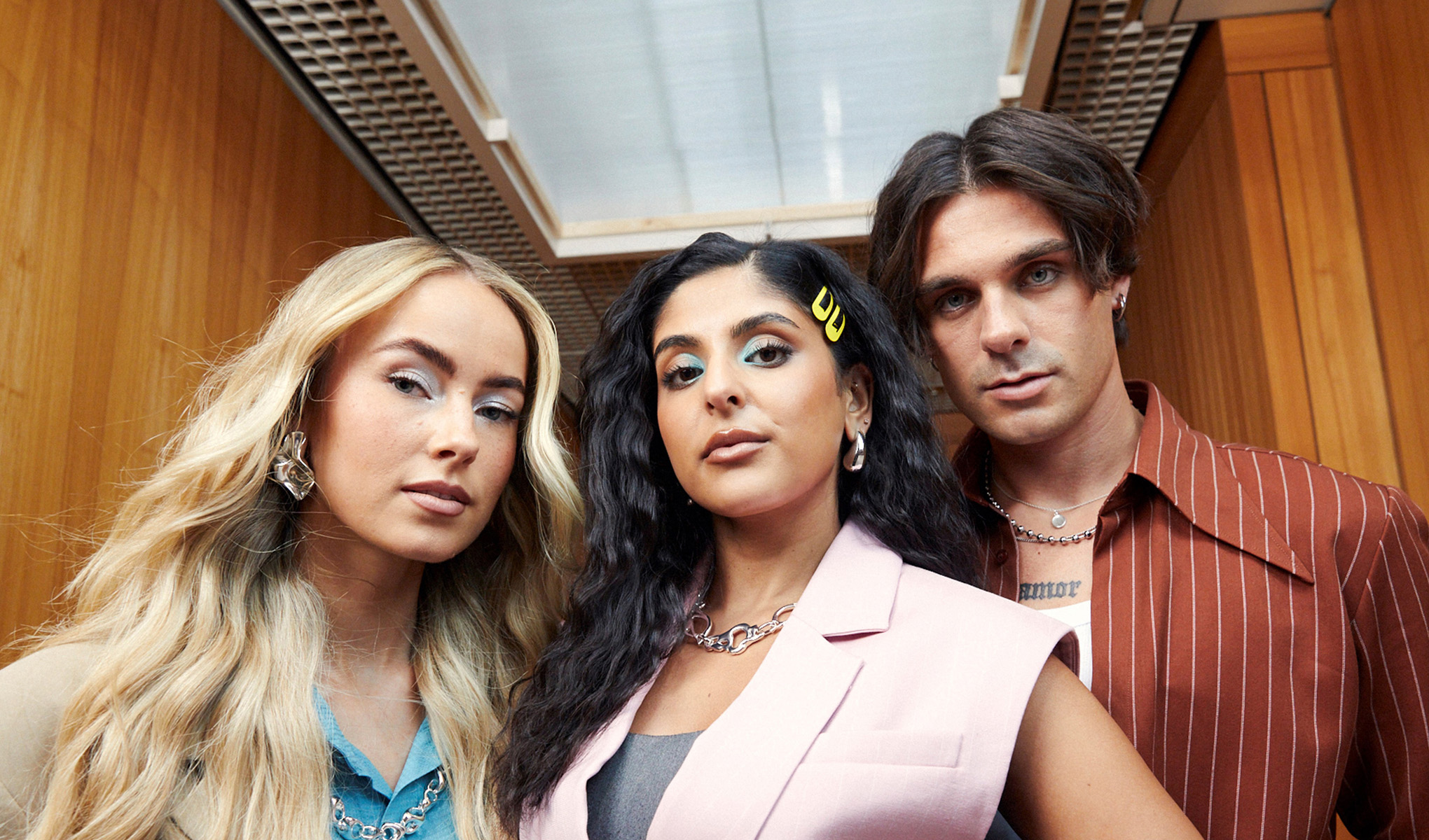 Kolme nuorta aikuista muotikuvassa sisätiloissa.