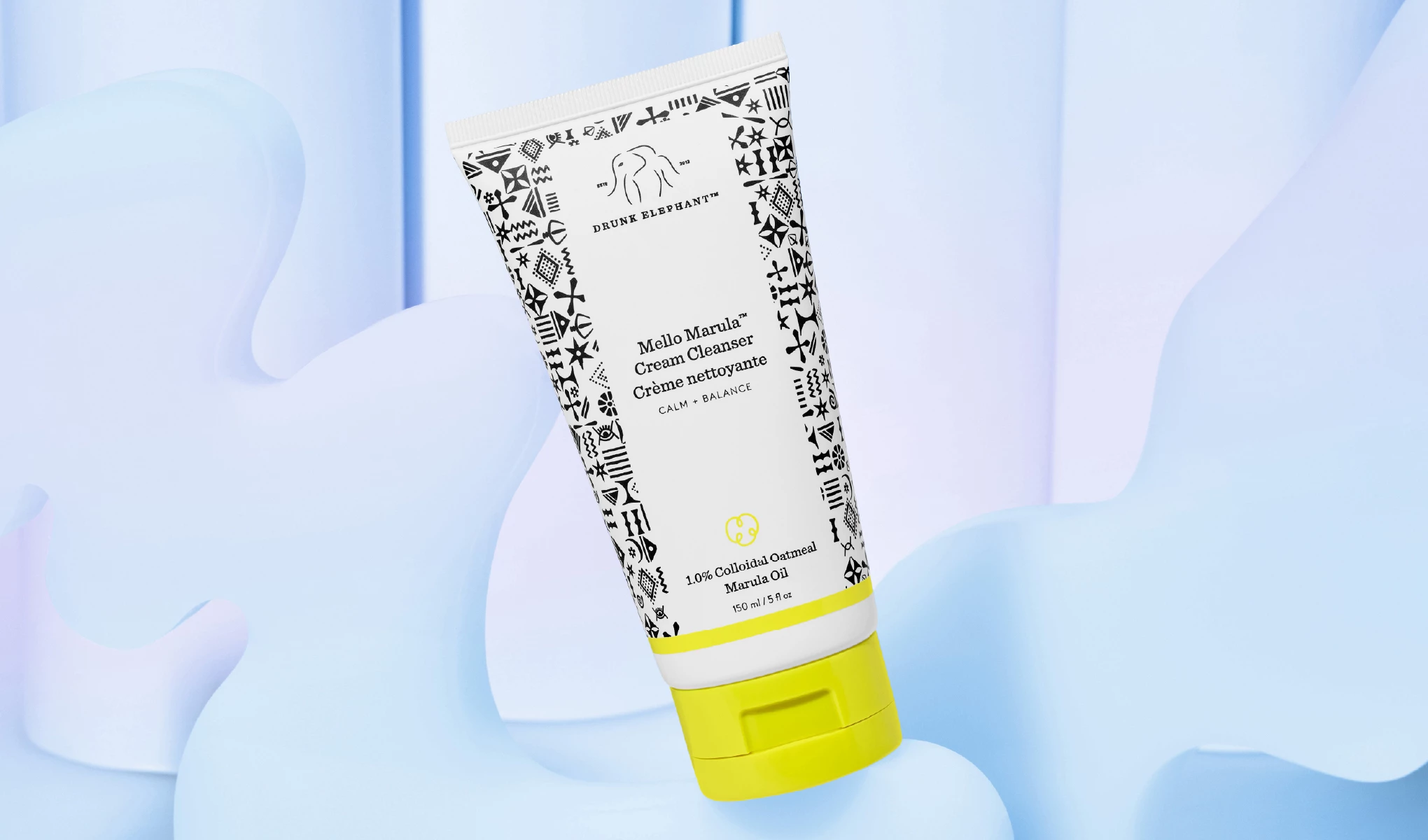 En tube med Drunk Elephant Mello Marula Cream Cleanser med svart-hvitt mønsterdesign og gul kork, plassert mot en lyseblå bakgrunn.