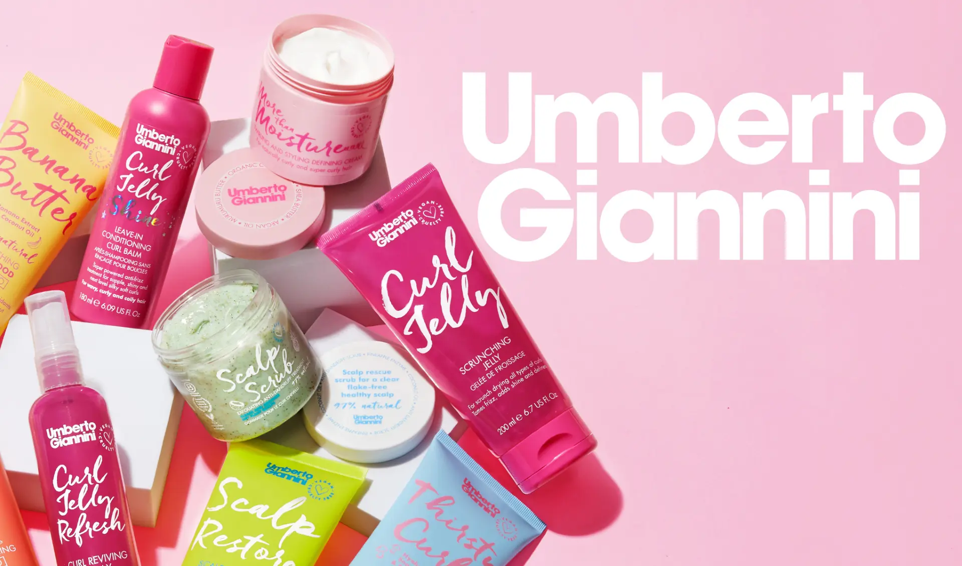 Umberto Giannini -hiustenhoitotuotteita vaaleanpunaisella taustalla. Mukana Banana Butter, Curl Jelly Shine, Scalp Scrub ja muita tuotteita.