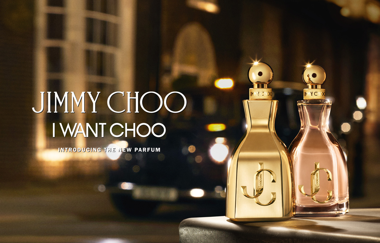 Kaksi Jimmy Choo -hajuvettä, toinen kullanvärinen ja toinen vaaleanpunainen, on sijoitettu pinnalle, jonka taustalla on sumea kaupunkikuva. Kuvan tekstissä lukee ”Jimmy Choo I Want Choo” ja ”Introducing The New Parfum”.