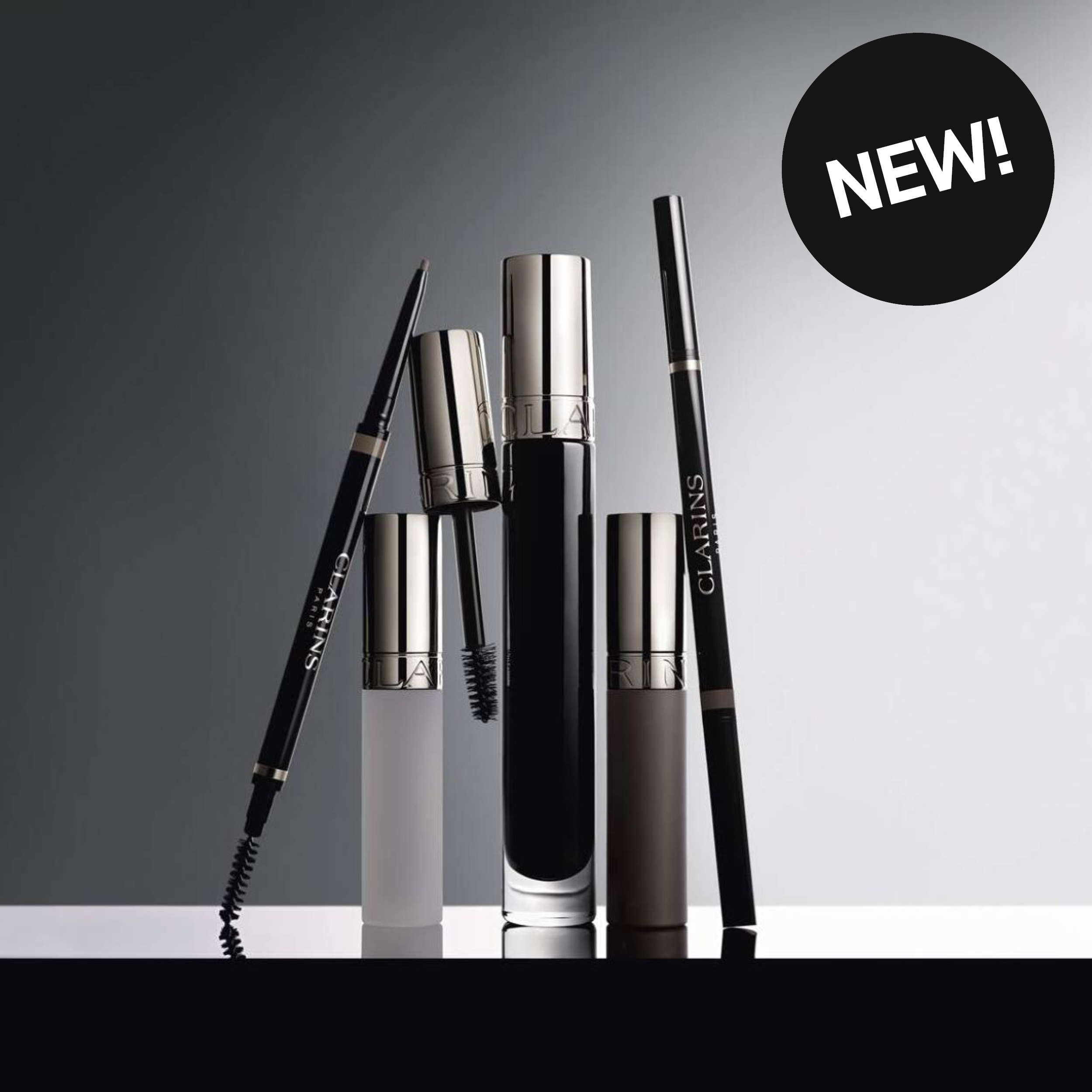 Produktbild med texten “NEW!” och Clarins ögonbrynspenna, mascara och bryngel i svart och silver mot mörk gradientbakgrund. Synlig text på produkterna inkluderar “CLARINS”.