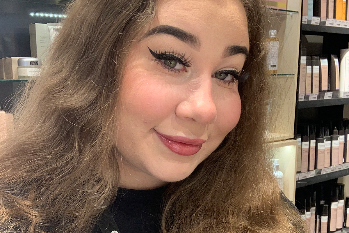 Person med langt, bølgete hår og naturlig sminke med markert eyeliner og rødbrun leppestift