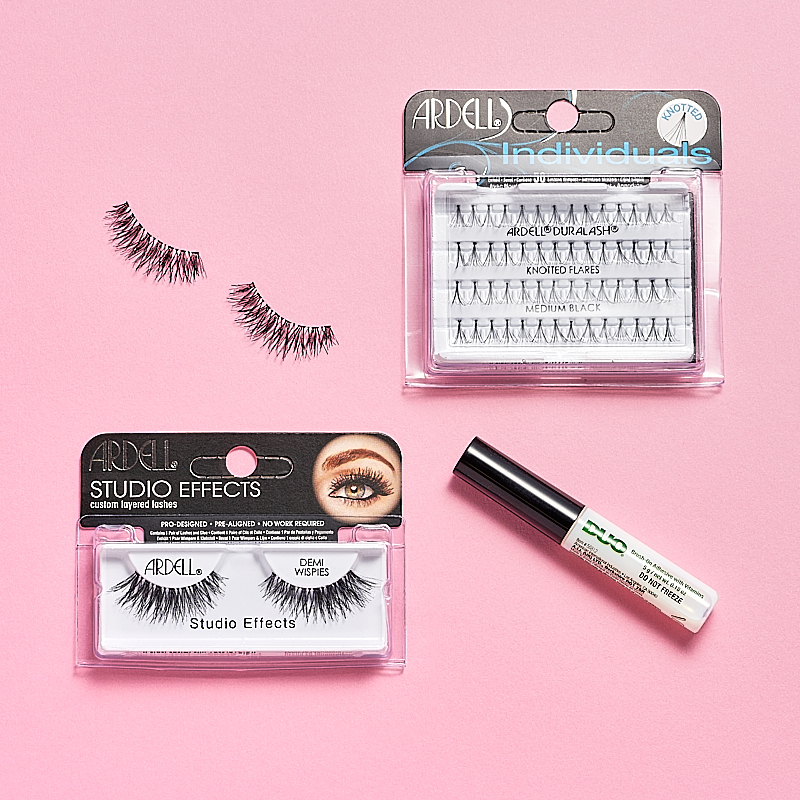 Lösögonfransprodukter från Ardell, inklusive Ardell Studio Effects Demi Wispies, Ardell Individuals Knot Flared Medium Black och en tub med DUO ögonfranslim. Produkterna är placerade på en rosa bakgrund.