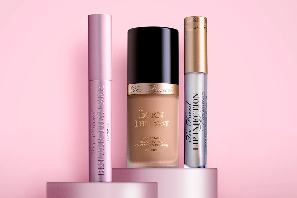 Kolme Too Faced -kauneustuotetta vaaleanpunaisilla korokkeilla vaaleanpunaista taustaa vasten.