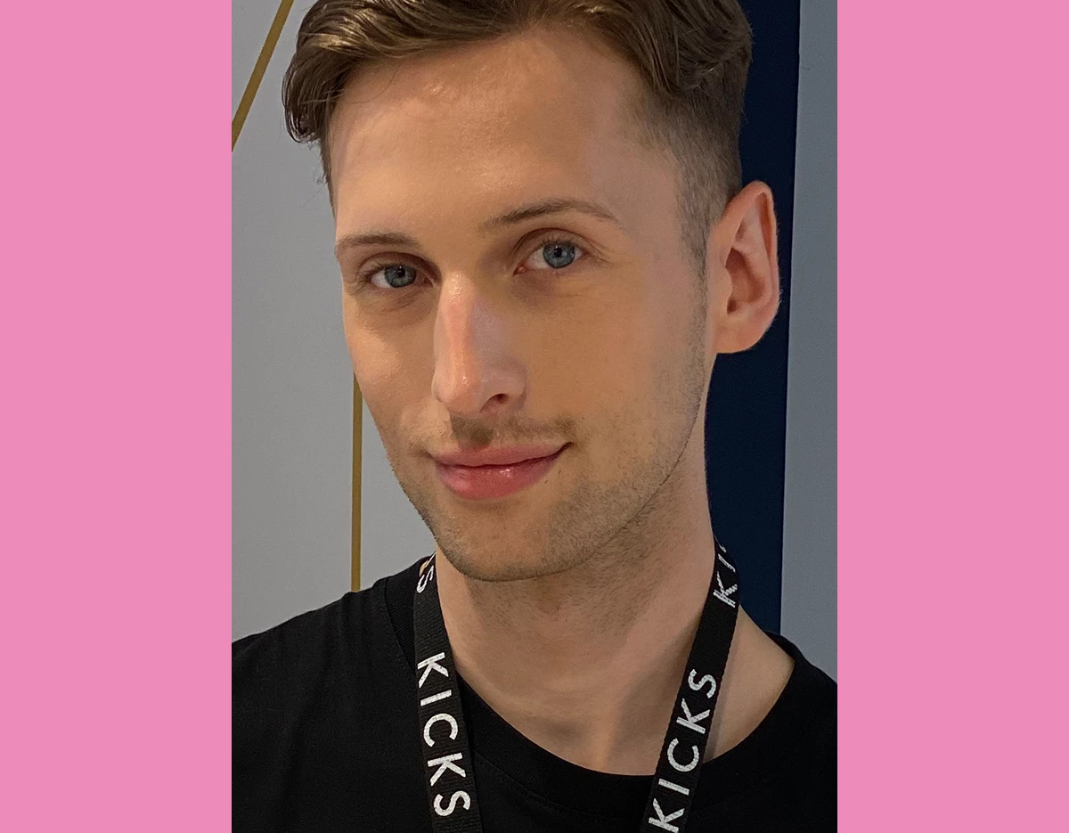 Mann i svart t-skjorte og sminke som smiler til kameraet, med en rosa ramme.