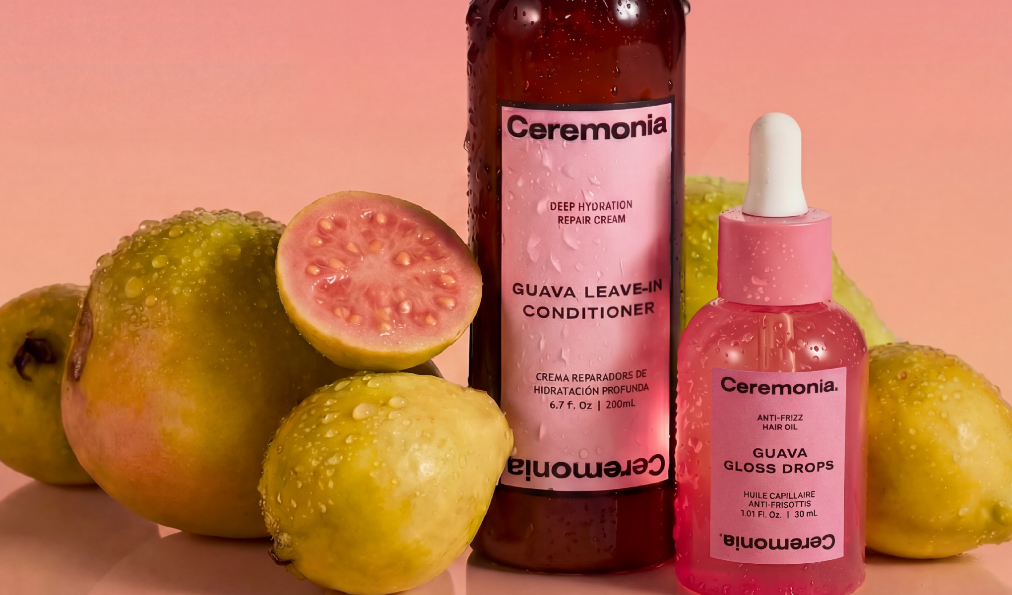 Ceremonia hårvårdsprodukter mot rosa bakgrund tillsammans med färska guavor och vatten-droppar på frukterna och förpackningarna. Synlig text inkluderar “Ceremonia”, “GUAVA LEAVE-IN CONDITIONER”, “DEEP HYDRATION REPAIR CREAM”, “GUAVA GLOSS DROPS” och “ANTI-FRIZZ HAIR OIL”.
