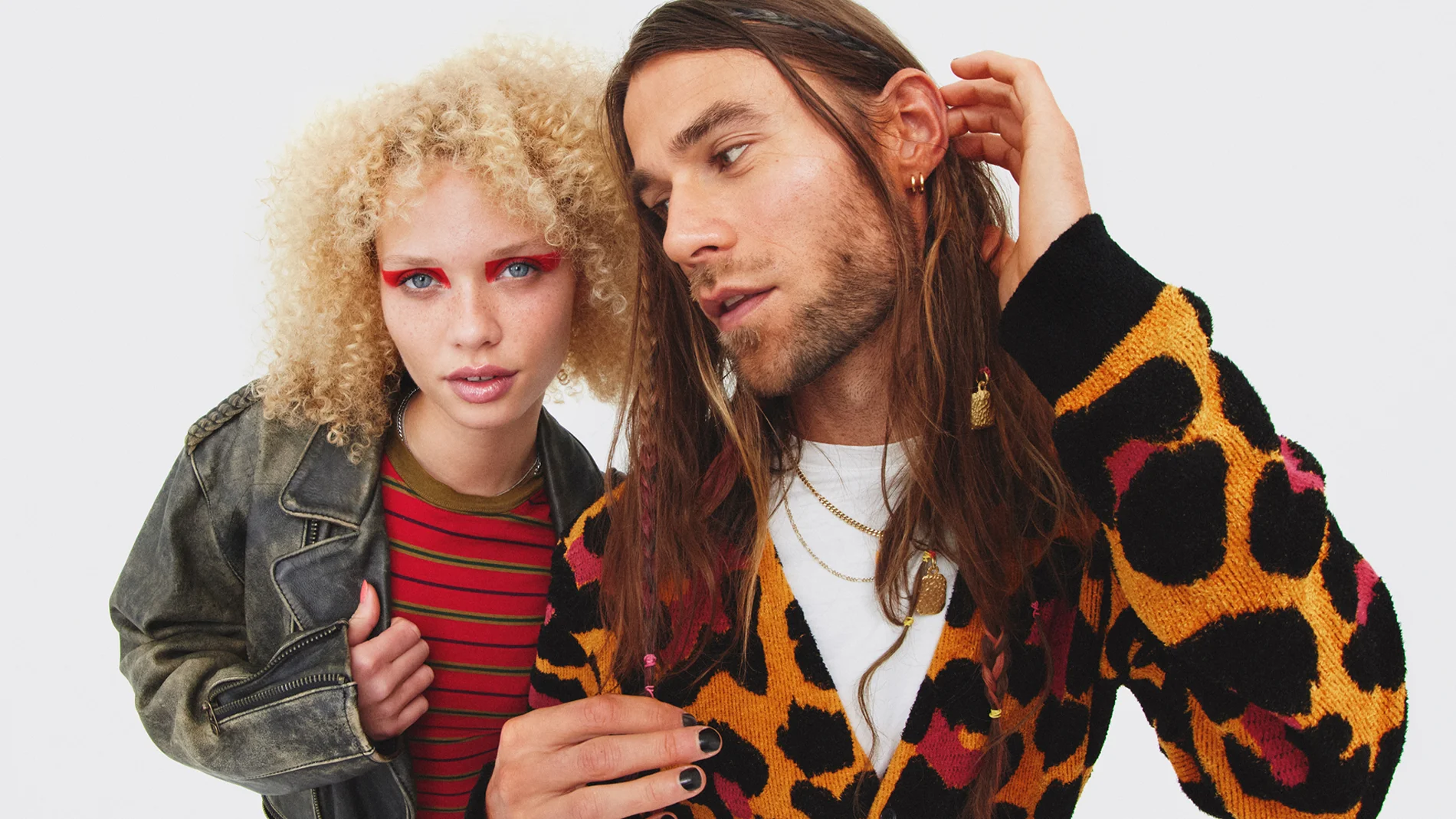 To personer poserer sammen, én med krøllete blondt hår og fargerik øyesminke og én med langt brunt hår og leopardmønstret cardigan.