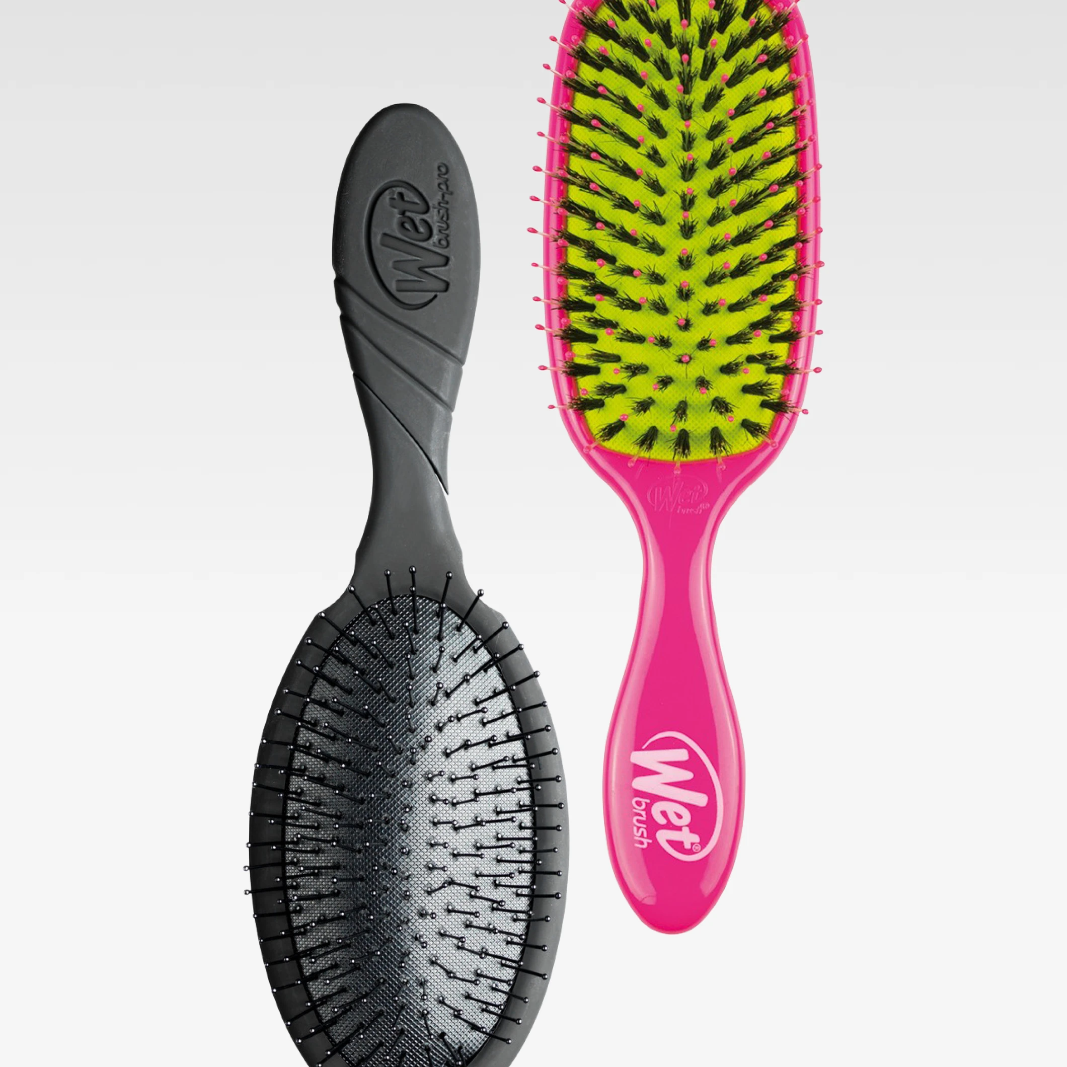 Kaksi Wet Brush -hiusharjaa vaaleaa taustaa vasten, yksi musta harja ja yksi pinkki harja keltaisella harjapohjalla. Kahvoissa näkyy brändin nimi “Wet brush”.