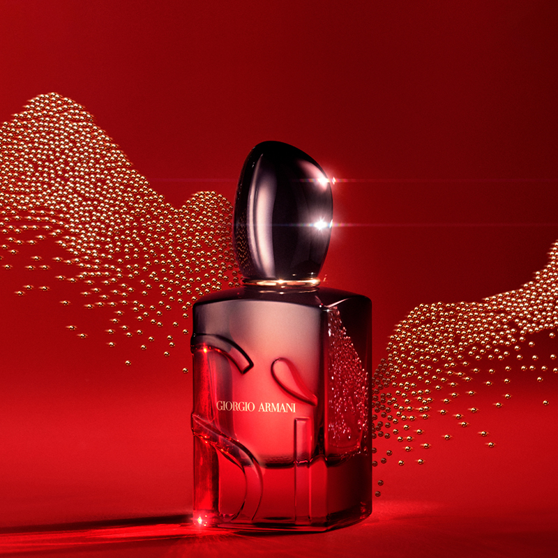 Parfymeflaske fra Giorgio Armani med teksten «Sì». Flasken er rød med mørk kork og har et elegant, buet mønster. Bakgrunnen er intens rød med gylne prikker som danner et bølgemønster.