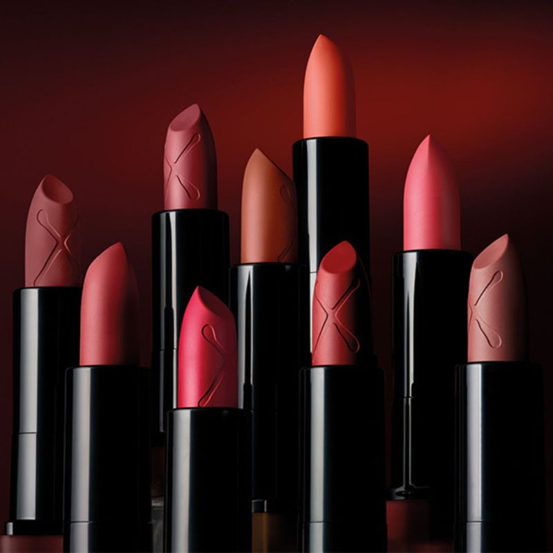 Flere leppestifter fra Max Factor i ulike nyanser av rødt, rosa og brunt, mot en mørkerød bakgrunn.
