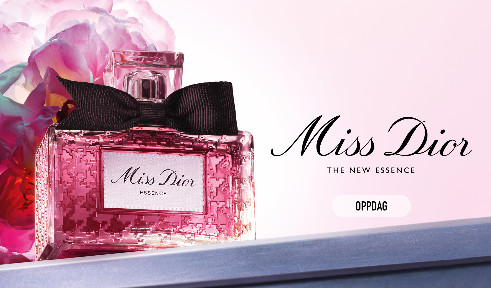 Miss Dior-parfyme, den nye Essence. I bakgrunnen vises bylandskapet. Flasken er rosa og har en svart sløyfe.
