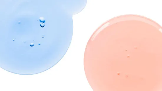 Nærbilde av to dråper væske på en hvit bakgrunn, en blå og en rosa.