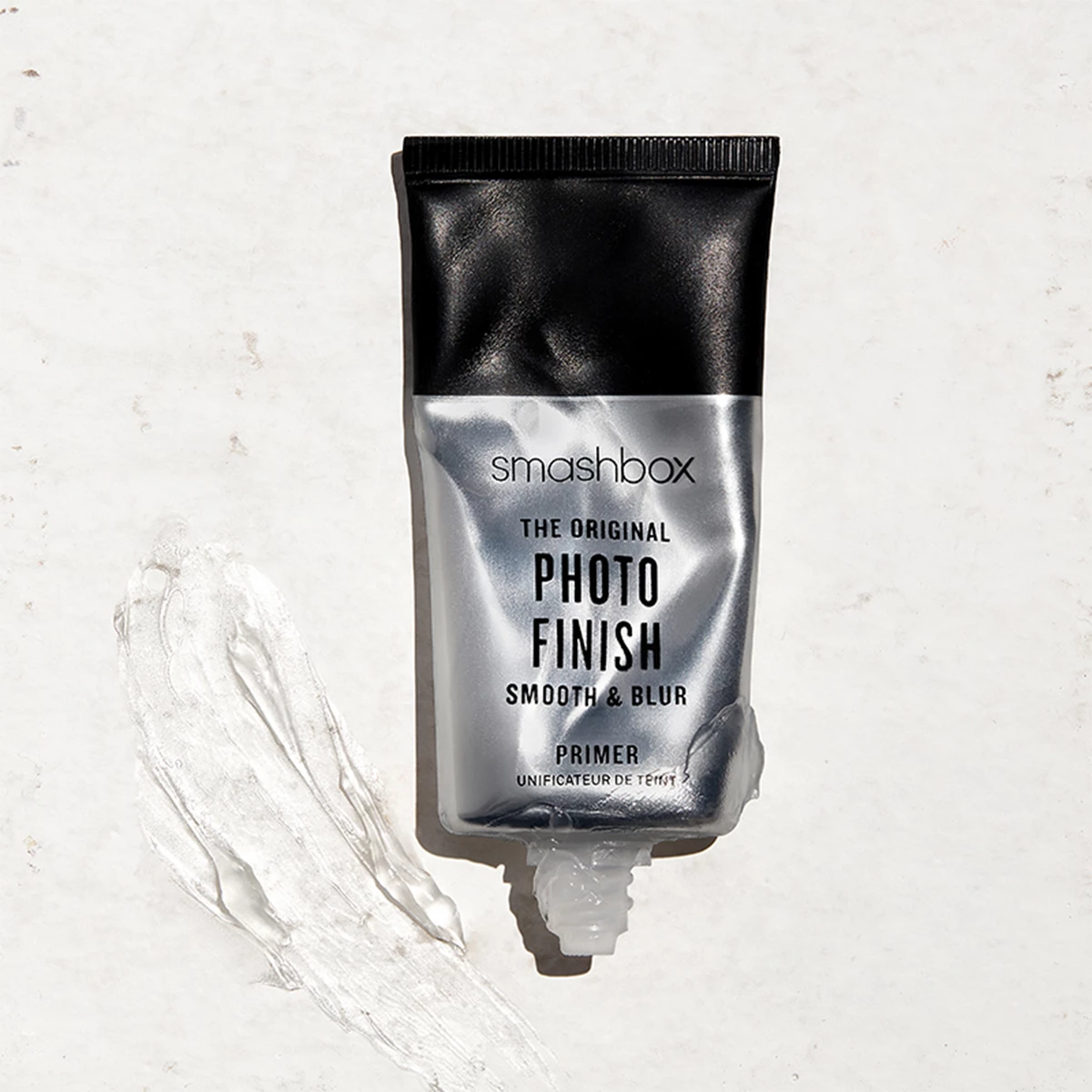 Smashboxin hopean ja mustan värinen tuubi asetettuna vaalealle alustalle. Pieni määrä pohjamaalia on puristettu ulos ja on tuubin vieressä. 