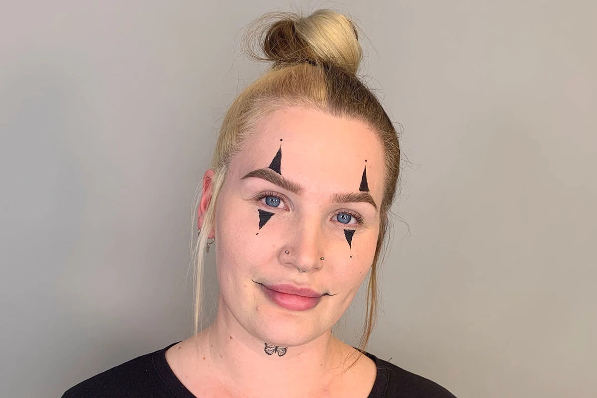 Kvinna med clownsmink som har svarta trianglar under ögonen och över ögonbrynen, samt längre dragna mungipor.