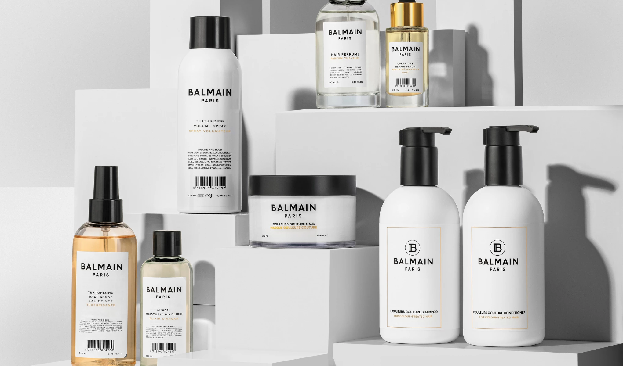 Balmain Paris hårvårdsprodukter i olika flaskor och burkar på vita podier.